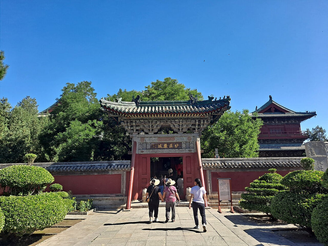 Visitors approaching a tiled gateway through a planted courtyard at Longxing Temple