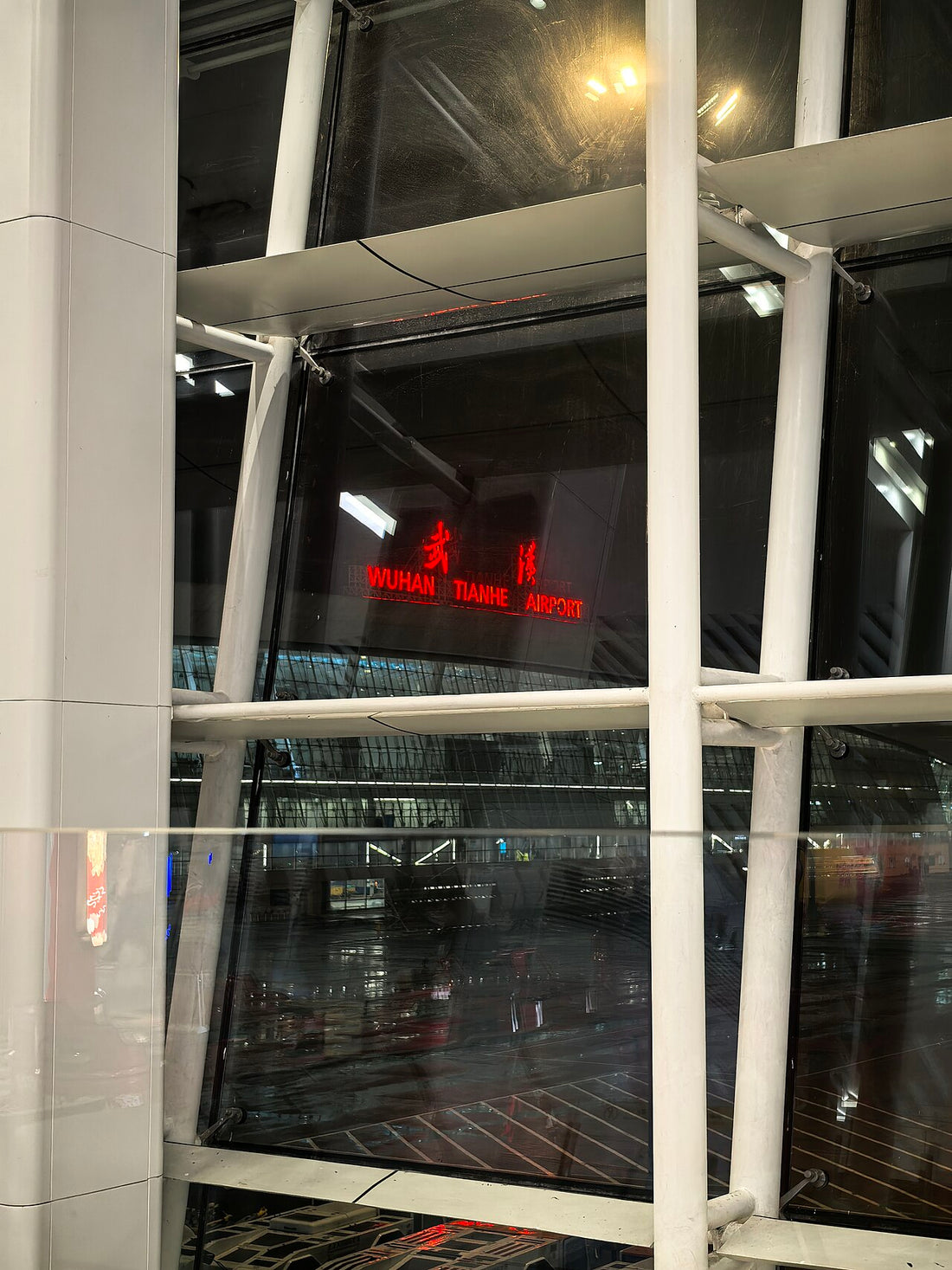 Illuminated Wuhan Tianhe Airport lettering viewed through a window at night