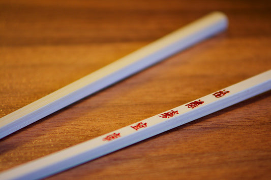 White chopsticks with red Chinese characters resting on a wooden table