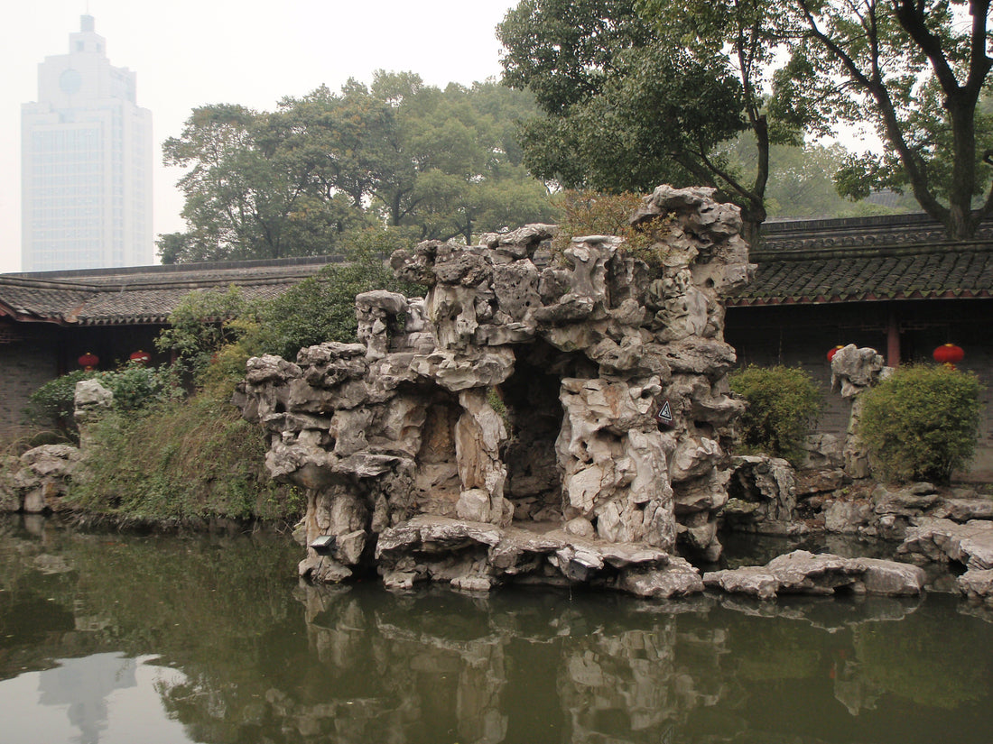 Garden rockery reflected in a pond beside tiled corridors at Tianyige Museum in Ningbo